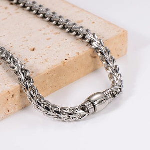 Polished stainless steel wheat chain necklace resting on a decorative beige stone