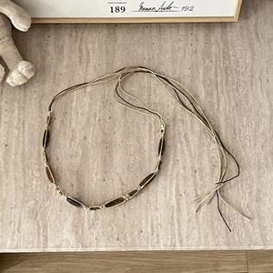 Close-up of bohemian woven belt with amber-like beads and cream rope on stone background