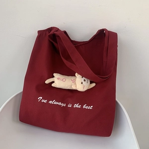 Detail of burgundy canvas tote bag with plush kitten doll charm and white printed typography