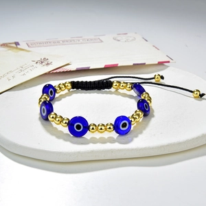 Detail of blue glass evil eye beads and gold spheres on a black woven bracelet