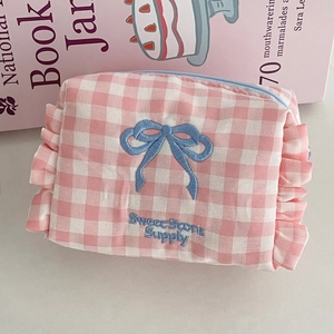 Detail of pink plaid makeup bag with blue ruffle edges and embroidered bow design