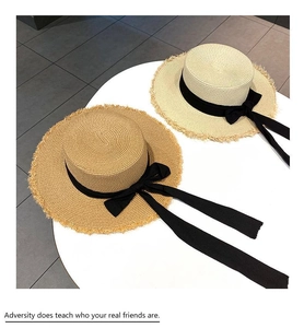 Detail of flat top straw boater hats in cream and camel with frayed edges and black ribbons