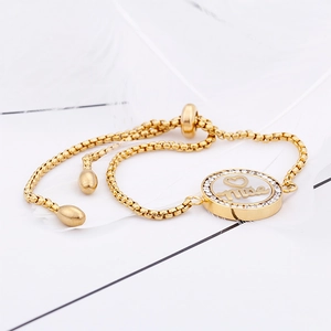 Macro detail of gold-plated adjustable bracelet with 'Nice' zircon pendant and white feather