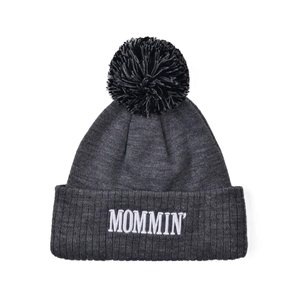 Detailed view of dark grey knit hat with large black pompom and MOMMIN embroidery