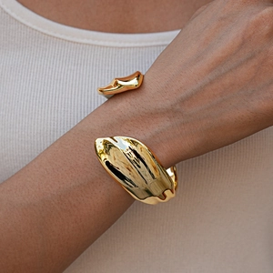 Close-up of a wide gold open cuff bracelet with glossy irregular organic textures