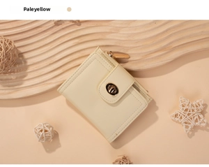 Detail view of a pale yellow leather wallet featuring a golden twist lock and zip pocket
