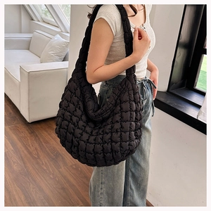 Quilted black cloud tote bag shown on shoulder in a bright minimalist indoor setting