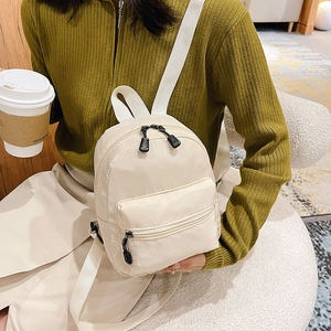 Beige nylon women's backpack with dual zipper compartments shown on a model