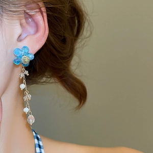 Macro shot of long flower earrings with blue crystal petals and pearl tassel on model