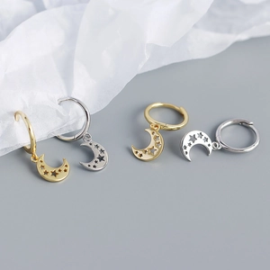 Macro detail of gold and silver moon earrings with hollow star patterns on a grey surface
