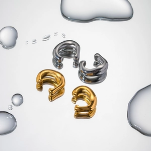 Artistic close-up of 18k gold and silver stainless steel rivet ear cuffs on water mirror