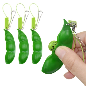 Detail showing a hand squeezing the green pea pod keychain to reveal a cute smiling face