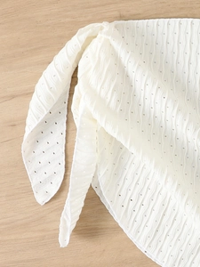 Detailed macro view of white textured bikini cover-up fabric with wave pleats and knot ties