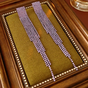 Détail de longues boucles d'oreilles à pompons en strass violets sur un support vintage