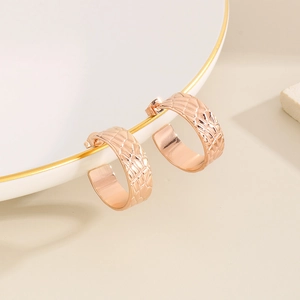Detail of rose gold C-shaped earrings with irregular textured surface on a white plate