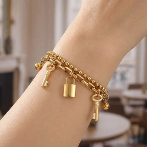 Detail showing gold double-layer chain bracelet with padlock and two key charms