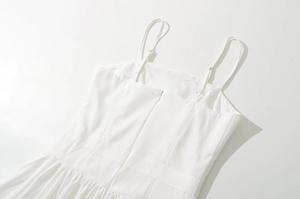 Close-up of white slip dress showing adjustable straps, zipper and pleated hem