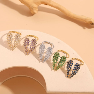 Close-up of five colorful leaf wing rings with zircon inlay on a soft beige stand