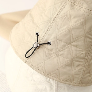 Detail of beige bucket hat featuring V-shaped quilting and black elastic drawstring adjustment