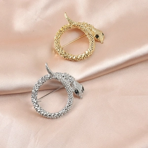 Elegant gold and silver coiled snake brooches displayed on soft pink silk fabric