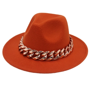 Detail of a bright orange fedora hat featuring a chunky gold acrylic chain decoration