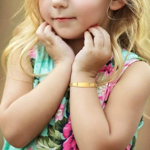 Detailed view of children's gold ID bracelet with customizable bar on a young girl's wrist