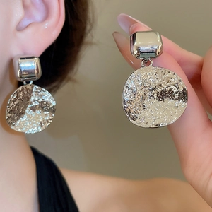 Detail of silver textured square and round pendant earrings worn on a model