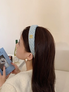 Dettaglio di un cerchietto in tweed azzurro con lettere dorate e perle