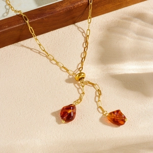 Golden stainless steel pull-chain necklace with amber resin pendants on sandy surface
