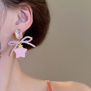 Close-up of pink beaded bow earrings with golden star pendant on female model