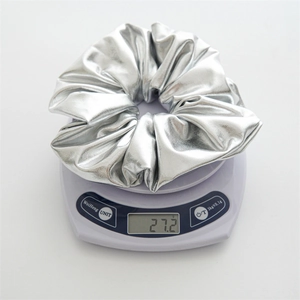 Macro shot of silver metallic hair scrunchie on electronic scale showing 27.2g weight
