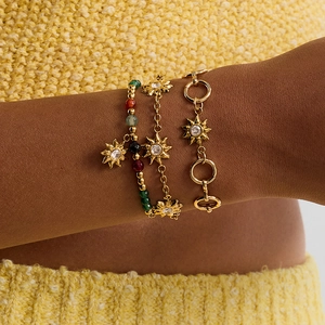 Close-up of gold sun bracelets with colored gems on model against yellow knitwear