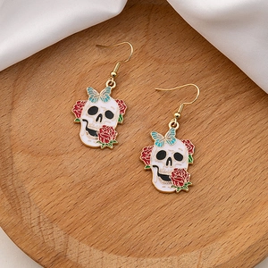 Detail of skull earrings with red roses and blue butterflies on a wooden tray