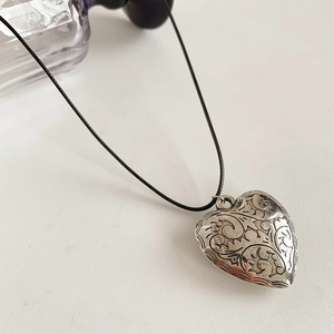 Detailed macro view of vintage heart pendant with intricate floral relief on black cord
