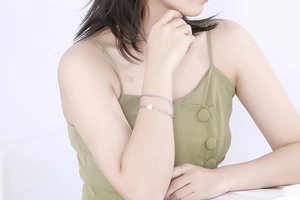 Detail of silver double-layered heart charm bracelet worn by a model on a green top