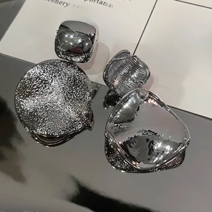 Vue macro de boucles d'oreilles géométriques argentées avec disque texturé et carré lisse