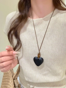 Detail showing a large black resin heart pendant on a brown cord necklace worn by a model