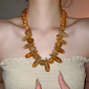 Close-up of oversized amber resin beads on a bohemian style necklace worn by a model