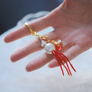 Detail of red tube bead tassel and heart charm with gold glitter on white pearl keychain