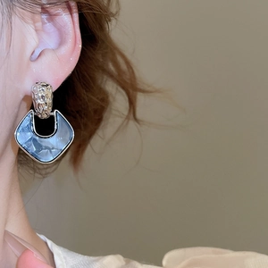 Close-up of geometric diamond-shaped earring with blue marble acrylic and textured metal