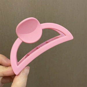 Primer plano de mano sosteniendo una pinza de pelo de flor rosa con acabado mate