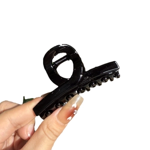Glossy black plastic shark hair claw clip held by hand for elegant French updo styling