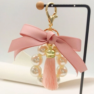 Detailed view of pink ribbon bow, pearl ring, and tassel on a golden metal keychain