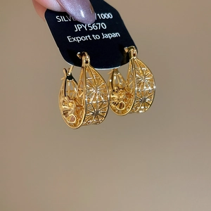 Detailed view of gold plated hollow flower hoop earrings on a black display card