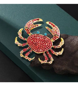 Macro detail of a golden crab brooch with red crystals on a dark textured background
