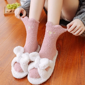 Pink coral fleece socks with dog embroidery and white plush slippers on wooden floor