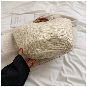 Detail of hand-woven straw tote bag with natural bamboo handle on neutral fabric