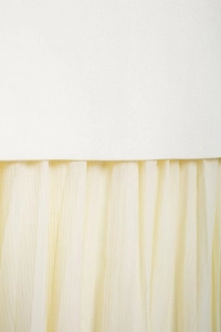 Detailed close-up of white knitted fabric stitched with beige pleated mesh skirt