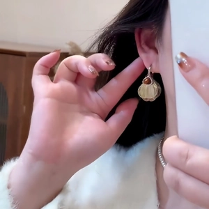 Close-up of shell-shaped gold earrings with brown stone inlay on model's ear
