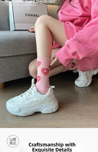 Detail of pink crew socks with red heart patterns worn with white platform sneakers